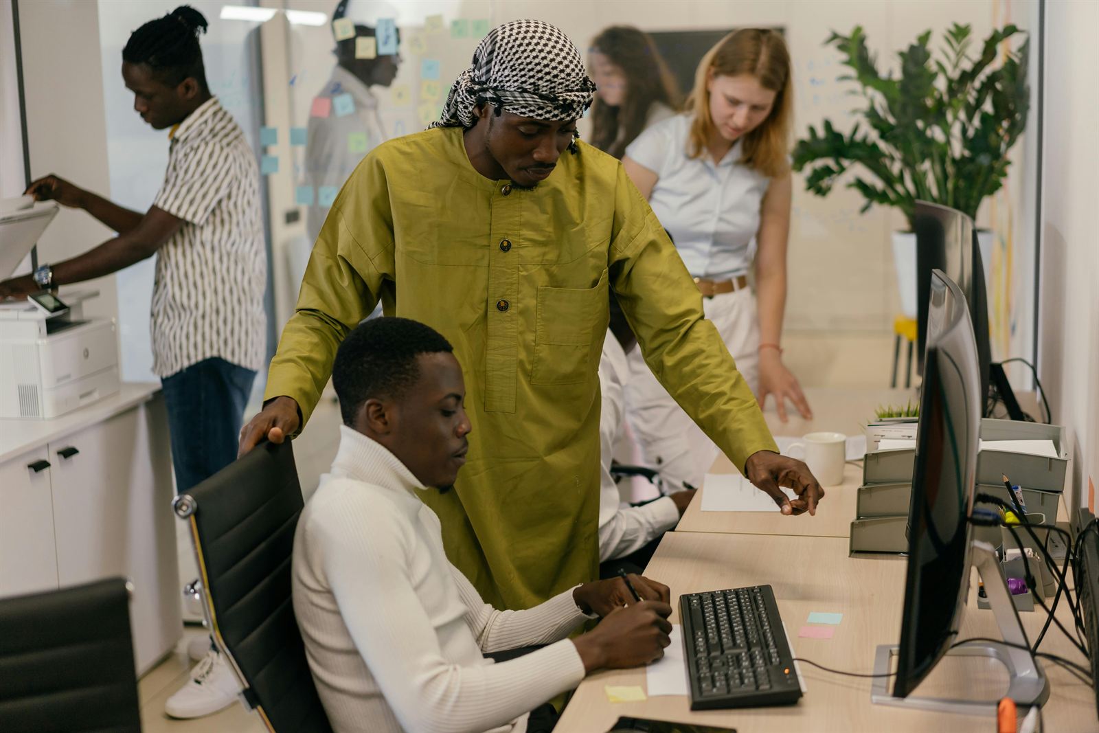 A colleague leaning in to coach another at their desk while the team works