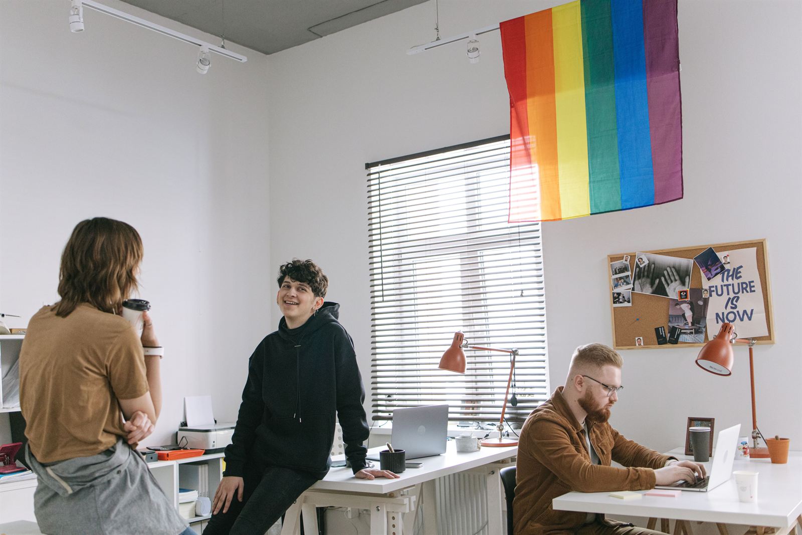 A modern startup office with a team at work beneath a sign reading the future is now