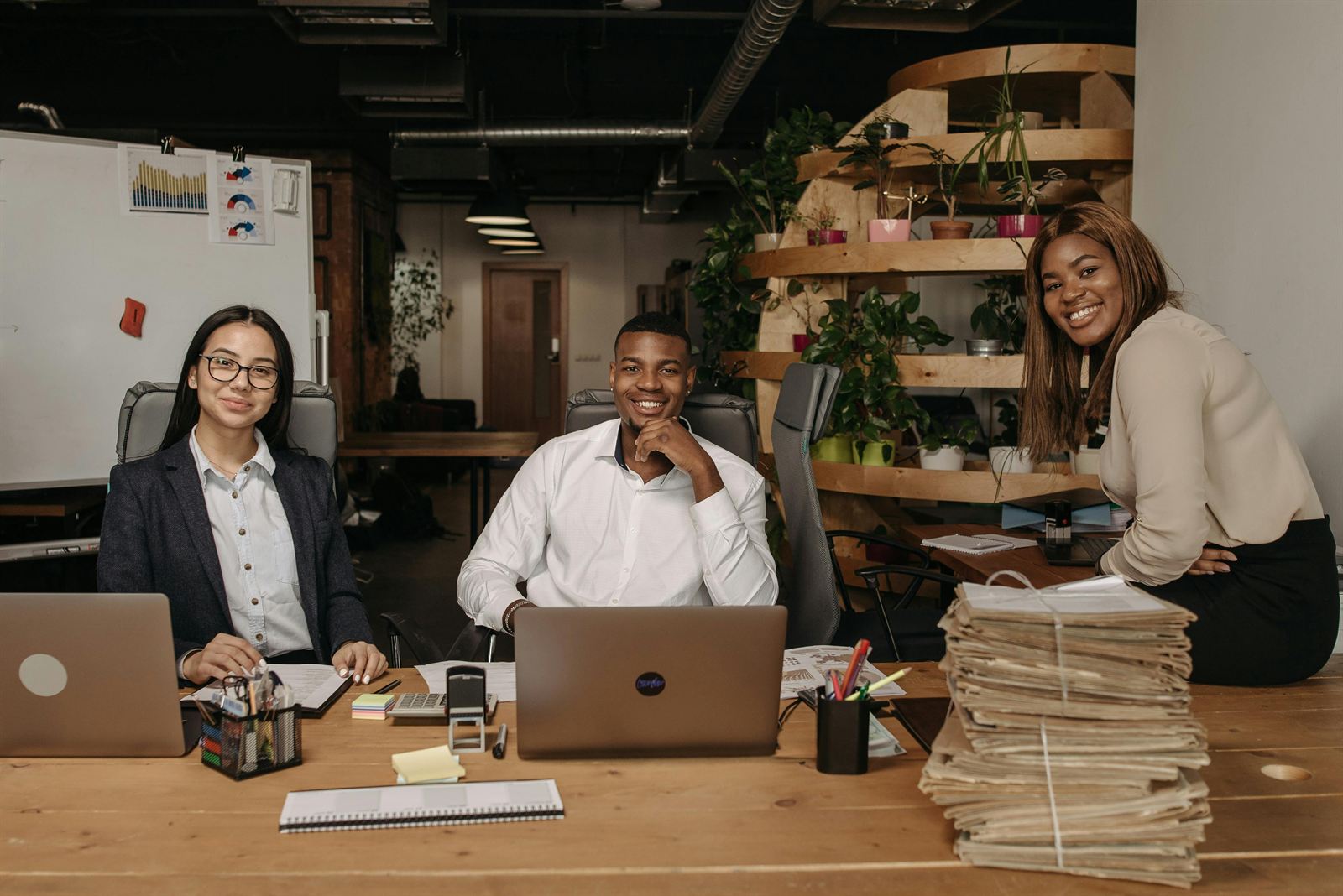 A confident team at their desks with laptops beside a stack of paper files
