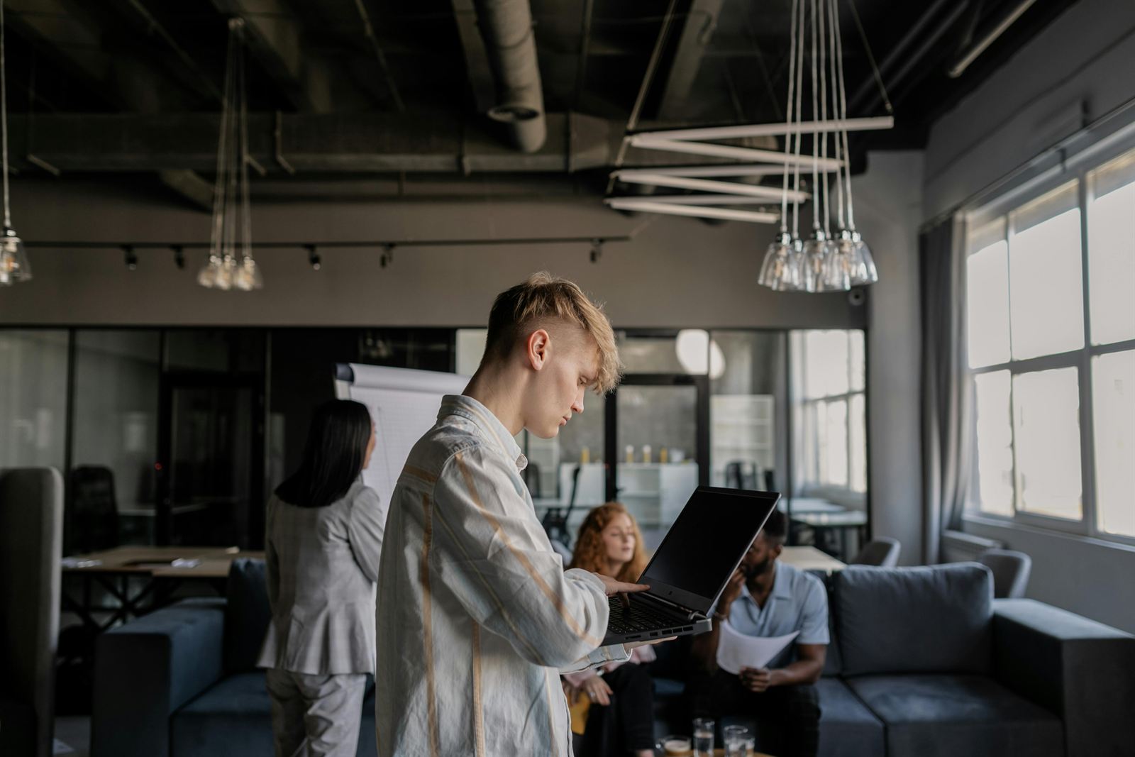 A young professional working on a laptop while colleagues collaborate behind